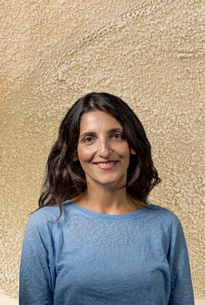 Anastasia Saltou in a blue shirt standing in front of a neutral wall, representing CORTEX Grid with a statement.