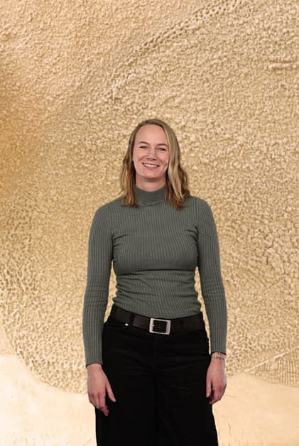 Janine Derix in a grey shirt standing in front of a neutral wall, representing Technical Communication with a statement.