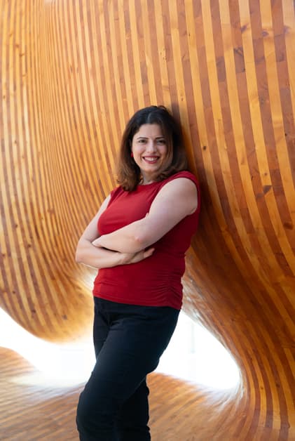 Maryam Khallaghi in a red shirt standing in front of a wooden wall, representing Process Management with a statement.