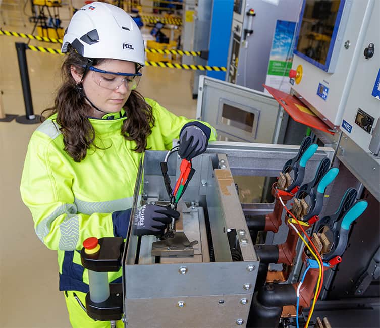 Technician in high-visibility gear working at a medium voltage circuit breaker, in a secure work zone.