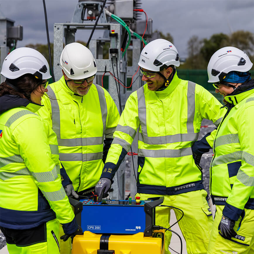 Team of engineers in high-visibility gear collaborating and laughing around the CPX 200 device in an substation.